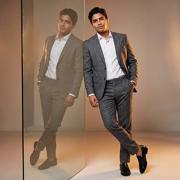 Stylized studio portrait in a grey plaid suit on reflective glass, warm rim lighting and corporate styling.