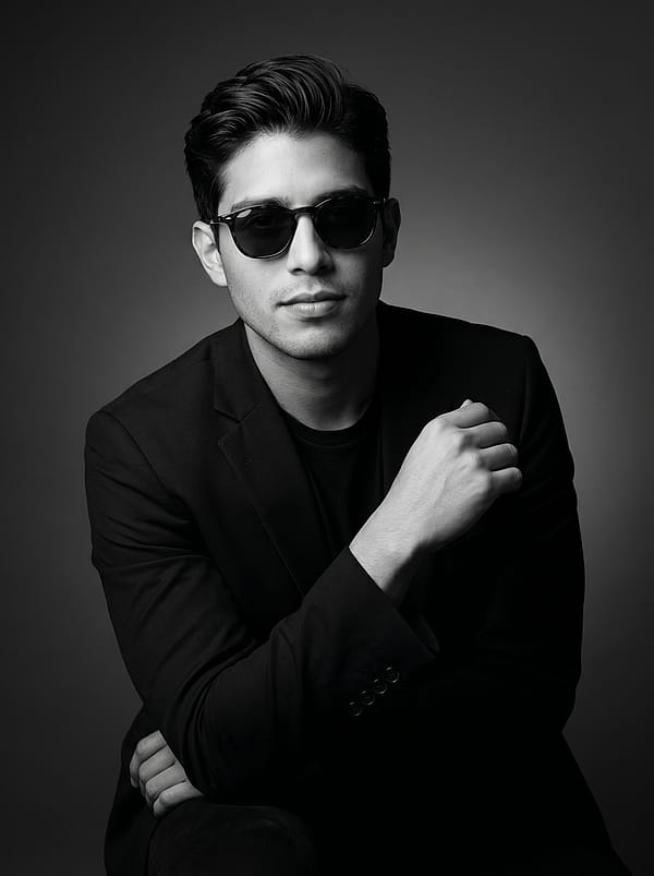 Black and white editorial portrait in a dark blazer with Rembrandt studio lighting, smooth gray backdrop.