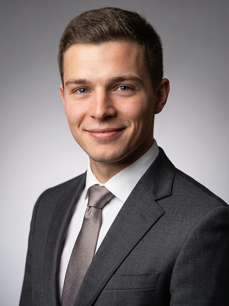 Clean professional portrait against soft gray gradient, three-quarter angle, natural expression, business attire.