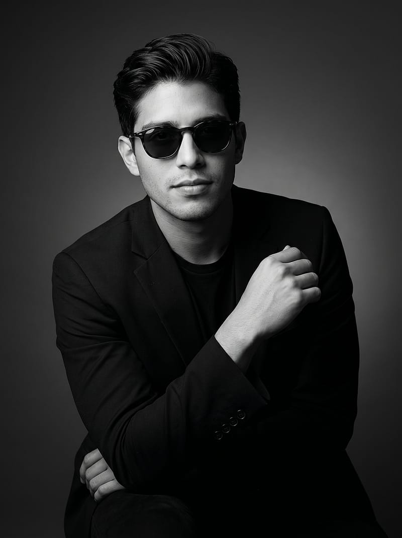 Black and white editorial portrait in a dark blazer with Rembrandt studio lighting, smooth gray backdrop.